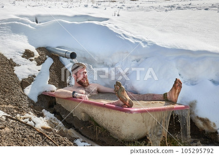 Taking cold plunge inmersing in a snowy bathtub 105295792