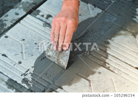 A carpenter repairs a building with tools at a construction site. The tiler lays out the tiles. Hand 105296154