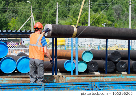 Slinger in hard hat and high-visibility vest unloads metal pipes for gasification on summer day in Slinger in hard hat and high-visibility vest unloads metal pipes for gasification on summer day in 105296205