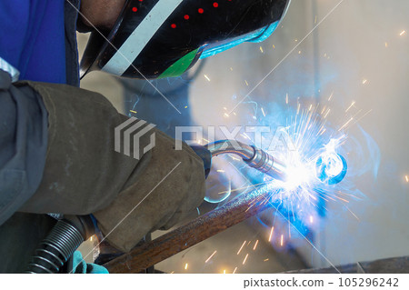 The welder works at the factory in the production workshop. a masked gas welder welds a metal pipe 105296242