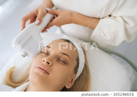 Close-up face of young woman receiving HUFU therapy high intensity ultrasound treatment on face. Cosmetologist doing non-surgical cosmetic plasma lift on female client with ultrasonic device. Close-up face of young woman receiving HUFU therapy high intensity ultrasound treatment on face. Cosmetologist doing non-surgical cosmetic plasma lift on female client with ultrasonic device. 105296658