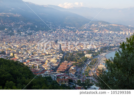 Enjoy the stunning view of Alanya from the observation deck, with lush trees, blue sea, and the iconic Lighthouse and Port of Alanya. The rocky peninsula adds a dramatic touch to the panoramic scene. 105299386