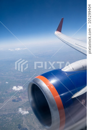 Airplane flight. Wing of an airplane flying above the clouds. View from the window of the plane. Airplane, Aircraft. Traveling by air. Aircraft's wing and land seen through the illuminator.  105299404