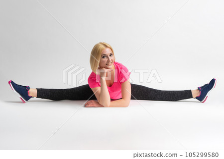 A woman in sportswear and sneakers sits in a transverse split A woman in sportswear and sneakers sits in a transverse split 105299580