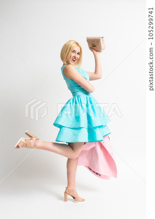 A woman in a blue elegant dress holds a pink coat and handbag in her hands A woman in a blue elegant dress holds a pink coat and handbag in her hands 105299741