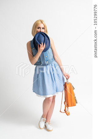 A woman in a blue summer dress with a backpack covers her face with a hat A woman in a blue summer dress with a backpack covers her face with a hat 105299776