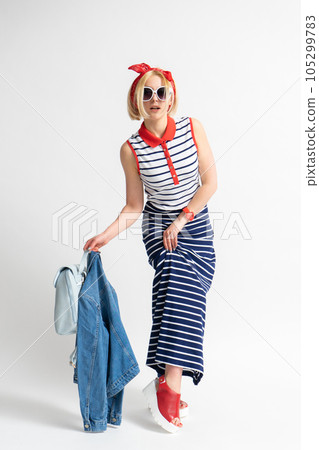 A woman with a backpack and a jacket in her hand lifts the hem of her dress, exposing her leg 105299783