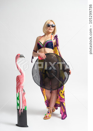 Woman in swimsuit with beach hat and sunglasses near figurine of flamingo 105299786