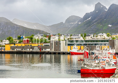Fishing boats at the pier with village houses and mountain in the background at Husoy village, Senja island, Norway 105301975