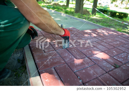 A worker aligns the gaps between the individual paving blocks. 105302952