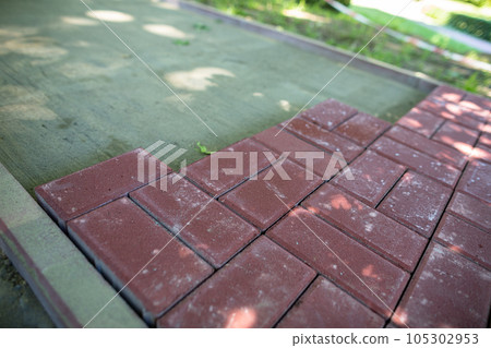 Unfinished pedestrian walkway made of rectangular red paving stones. 105302953