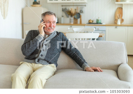 Happy middle aged senior man talking on smartphone with family friends. Older mature grandfather with cell phone talking with grown up children, resting at home. Older generation modern tech usage Happy middle aged senior man talking on smartphone with family friends. Older mature grandfather with cell phone talking with grown up children, resting at home. Older generation modern tech usage 105303093