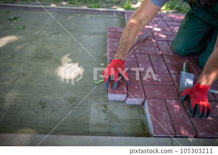 A worker lays red paving stones on an evenly prepared surface. 105303211