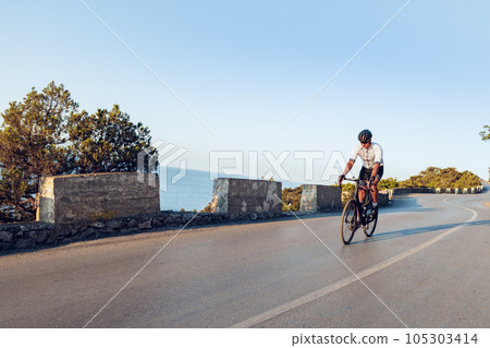 Man cyclist pedaling on a road bike outdoors in sun set 105303414