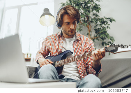 Man playing electric guitar and recording music into laptop 105303747