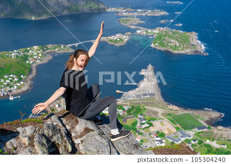 Happy young girl hiker enjoys the view on cliff edge of lofoten islands, in Norway, Reinebringen 105304240