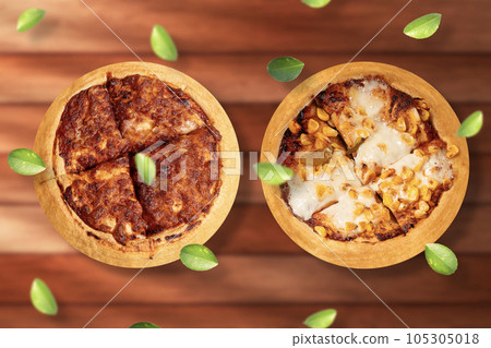 Two delicious hot Indian pizzas on wooden table. Margherita pizza and corn pizza with flying green leaves. top view Two delicious hot Indian pizzas on wooden table. Margherita pizza and corn pizza with flying green leaves. top view 105305018