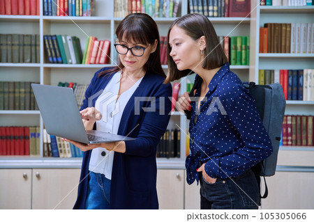 Female teacher with young college student talking while looking at laptop together, in library Female teacher with young college student talking while looking at laptop together, in library 105305066