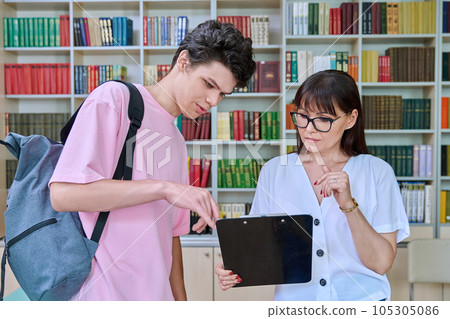 Middle-aged female teacher talking to male college student inside library Middle-aged female teacher talking to male college student inside library 105305086