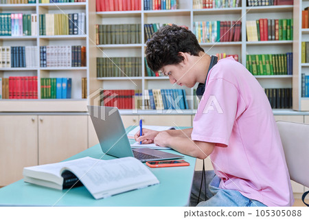 Young male student sitting with laptop with books in college library 105305088