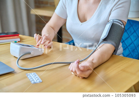 Middle-aged woman sitting at home, measuring blood pressure with tonometer 105305093