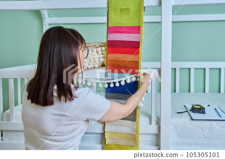 Woman designer choosing fabrics and textile accessories for decorating children's room 105305101