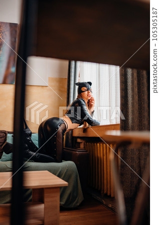 Playful attractive sexy young woman in black leather cat suit on the couch 105305187