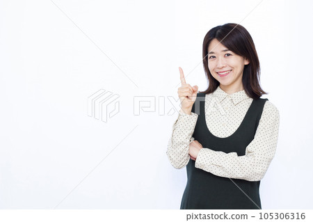 A woman in her thirties who raises her index finger in front of a white background 105306316