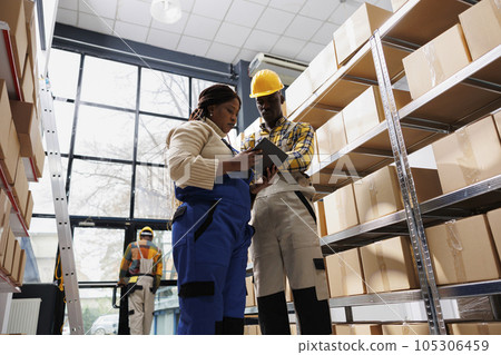 Warehouse workers looking at inventory data on digital tablet screen while standing in stockroom. African american logistics manager showing colleague goods storage management application 105306459