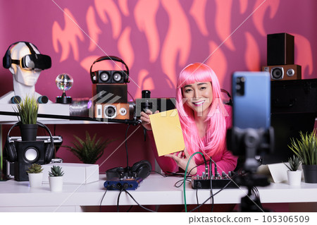 Smiling asian content creator holding notebook presenting school product in front of phone camera while filming review in broadcast studio. Influencer live streaming using vlogging equipment Smiling asian content creator holding notebook presenting school product in front of phone camera while filming review in broadcast studio. Influencer live streaming using vlogging equipment 105306509