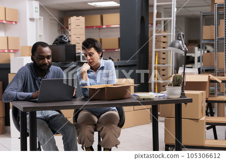 Employees looking at cargo stock on laptop after finishing packing trendy clothes in carton boxes before delivering to clients working in warehouse. Concept of heavy industry manufacturing factory. 105306612