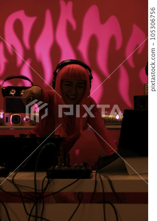 Artist with pink hair wearing headset while playing techno song at professional mixer console, enjoying night life in studio with pink background. Asian dj performing electronic music in club 105306756
