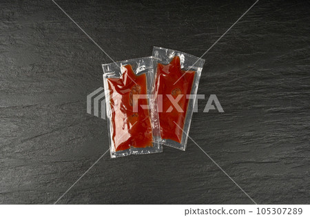 Ketchup in Square Plastic Bag on Black, One-Time Portion Transparent Catsup Sachet, Hot Tomato Sauce 105307289
