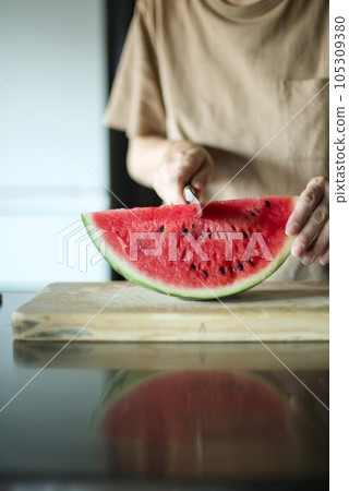 Cutting a watermelon on a cutting board with a knife 105309380