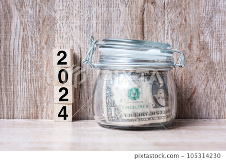 2024 Happy New Year with US dollar money glass American on wood table background. business, investment, retirement planning, finance, Saving and New Year Resolution concepts 105314230