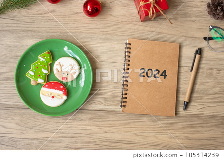 2024 notebook, black, Christmas cookies and pen on wood table, Top view and copy space. Xmas, Happy New Year, Goals, Resolution, To do list, Strategy and Plan concept 105314239