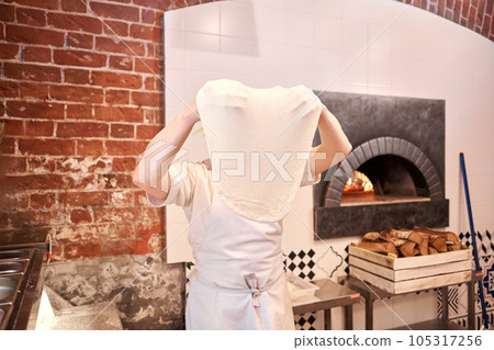 The chef prepare pizza. Raw pizza ready to bake. Cook in a apron in the kitchen Rolls out pizza dough. boxes for food delivery on background. 105317256