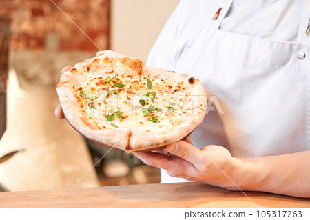 The chef holds a pizza in his hands. Neapolitan pizza from a wood-fired oven. Pizza is on the plate. Pizza with pear and gorgonzola. Fast delivery of food.  105317263