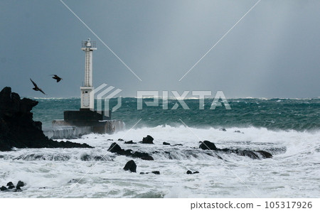 A lighthouse standing on a rough beach during a storm 105317926