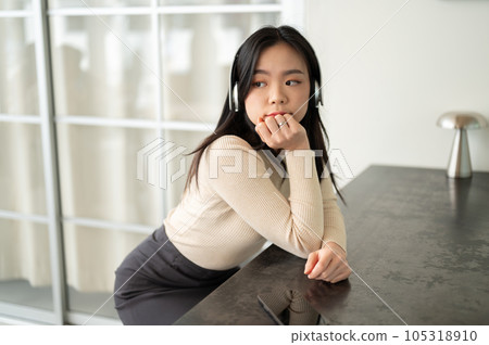 A calm Asian woman listening to music through her headphones while sitting at a table 105318910