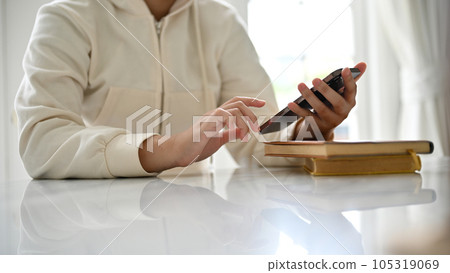 Close-up image of a woman in a comfy sweater using her smartphone at a table Close-up image of a woman in a comfy sweater using her smartphone at a table 105319069