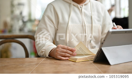 Cropped image of a woman reading a book and working on her project on her digital tablet Cropped image of a woman reading a book and working on her project on her digital tablet 105319095