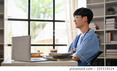 A professional Asian man doctor in scrubs is reading medical cases and research on his laptop A professional Asian man doctor in scrubs is reading medical cases and research on his laptop 105319524