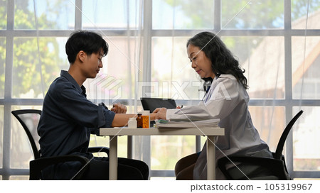 A sick young Asian male patient has a medical appointment to check up with a doctor at a hospital. 105319967