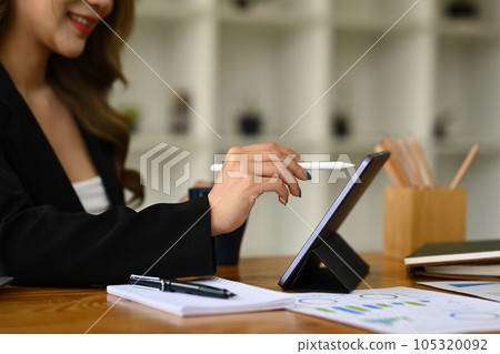 Side view of female analyst using stylus pen writing on digital tablet, working with financial graph, statistics document at workplace Side view of female analyst using stylus pen writing on digital tablet, working with financial graph, statistics document at workplace 105320092
