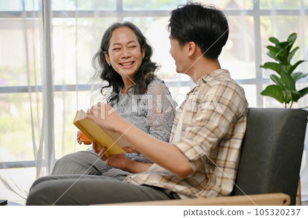 A happy Asian grandmother is laughing while talking and reading a book with her grandson 105320237
