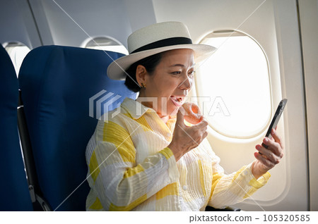 A happy female passenger enjoys eating doughnuts and using her smartphone during the flight 105320585