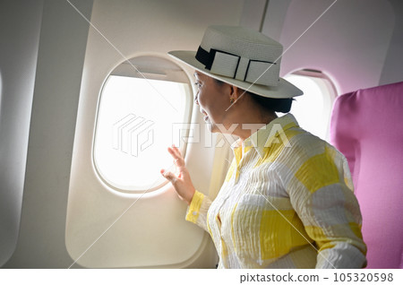 An excited and happy senior Asian female passenger is looking at the view outside of the plane 105320598