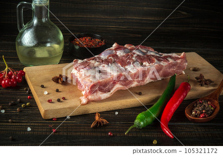 Fresh raw pork ribs on a kitchen cutting board with spices, oil and hot peppers. Cooking delicious food or grilling 105321172