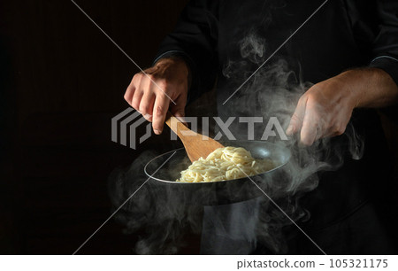 Cooking spaghetti in a frying pan in the hands of a chef. Space for advertising on a black background 105321175